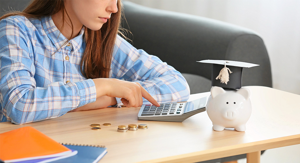 Four_Financial_Tips_Content young adult looking at calculator with a piggy bank with a graduation cap